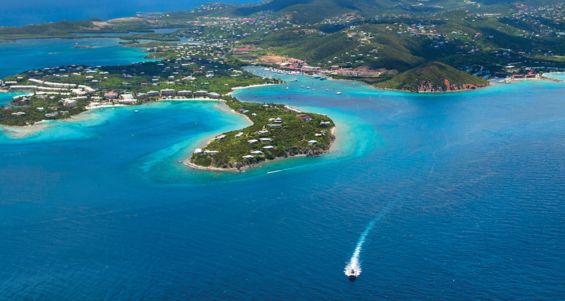 Aerial view of a tropical island with clear blue waters and a boat in the foreground.