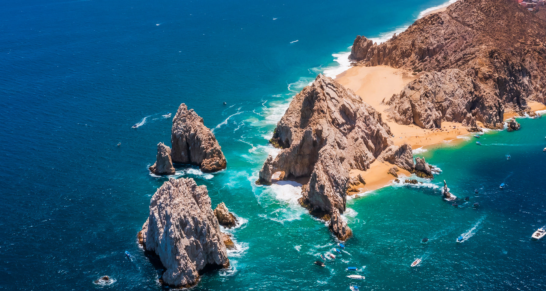 Aerial view of rocky coastline with blue ocean and sandy beach.